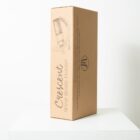Cardboard packaging with Crescent Wine Bottle Holder printed on it. The box features an illustration of a curved wine bottle holder. It is placed on a white, minimalistic surface with a plain background.
