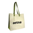 A beige tote bag with green handles and sides features the word aetna printed in black on the front.