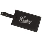 A black leather luggage tag with the word Coopers embroidered in white script. The tag features white stitching around the edges and has a black strap with a silver buckle for attachment.