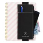 A spiral notebook with pink and white diagonal stripes, featuring a black pouch branded with a Mercedes-Benz logo. The pouch holds a blue pen and a partially visible mobile phone and currency notes.