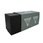 A dark green cardboard box with a black end is partially open, revealing a black interior box. The box features illustrations of two martini glasses and a 300 ml label. A white sticker with a colorful logo is on top.