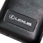 Close-up of a black leather item featuring a rectangular metal plate engraved with the Lexus logo and name in silver.