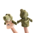 Two hands are holding green crocodile hand puppets against a white background. The puppets have big snouts and friendly expressions, featuring an embroidered patch on their chests.