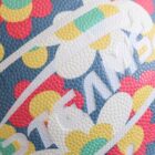 Close-up of a basketball with a colorful floral pattern in red, yellow, and green on a dark blue background. White text partially visible across the surface.