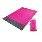 A pink and gray picnic blanket folded neatly beside its matching storage bag. The blanket is primarily pink with a gray border, and the storage bag is pink with a drawstring closure.