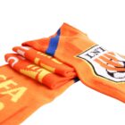 Folded orange scarf featuring a sports logo with a shield design and text. The scarf also has blue stripes and assorted patterns in yellow. The design appears bold and vibrant.
