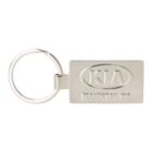 Rectangular metallic keychain with an engraved KIA logo inside an oval on the front. Below the logo, theres additional text. A circular keyring is attached to the short side of the rectangular piece.
