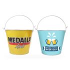 Two metal buckets with handles. The left bucket is yellow with Medalla Light text. The right bucket is blue with illustrations of clinking beer mugs and the text International Beer Day.