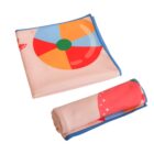 A folded beach towel with colorful prints including a beach ball and starfish. One towel is laid flat, featuring a blue trim, while another is rolled up beside it. The background is white.