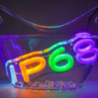 A clear bowl partially filled with water contains illuminated, colorful numbers IP68. The numbers are glowing in vibrant shades of orange, green, blue, and purple. The background is dark, enhancing the neon effect.