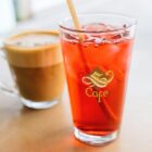 A glass of iced red drink and a cup of coffee on a table at a café.