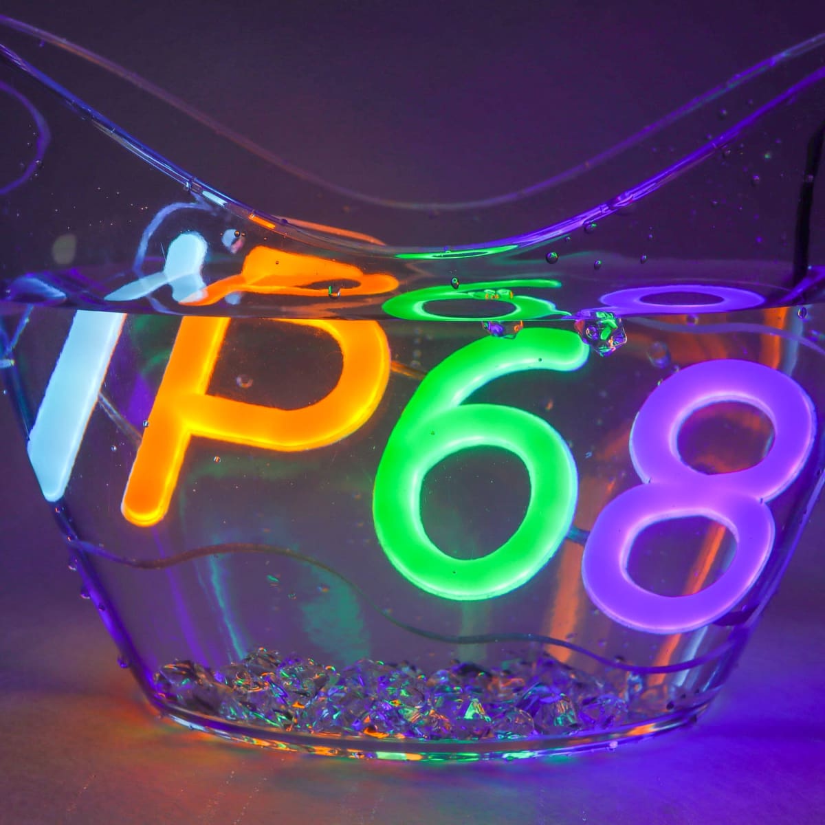 Illuminated letters and numbers IP68 in neon colors submerged in a clear bowl of water, surrounded by bubbles. The lighting creates a vibrant, glowing effect, emphasizing the waterproof rating concept.