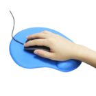 A hand rests on a black computer mouse placed on a blue mouse pad with an ergonomic wrist support. The mouse pad has a curved, kidney-shaped design to provide comfort while using the mouse.
