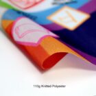 Close-up of a colorful printed fabric showing orange, pink, purple, and blue sections. The text 110g Knitted Polyester is visible below the fabric, indicating the material and weight.