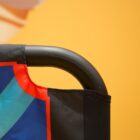 Close-up of a fabric banner with black edging and a vibrant blue and red geometric design on it. It hangs over a black metal frame against an orange background.