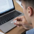 Person holding an Enzo 4Gb Key Flash Drive near a laptop with a document on the screen.