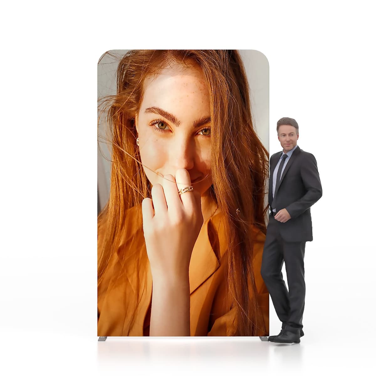 A man in a suit stands next to a large vertical display featuring a close-up photo of a woman with long hair, wearing a yellow top and smiling with her hand partially covering her mouth. The background is plain white.