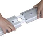 Hands demonstrating the connection of two metal tracks with a sliding mechanism, featuring visible screws and brackets. The background is plain white.