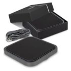 A sleek, black wireless charging pad is displayed with its open box and a braided USB cable. The charging pad has a rectangular shape with rounded edges and a simple design.