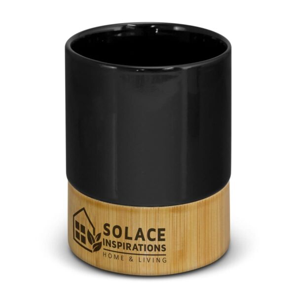 A black ceramic mug with a light wooden base featuring the text Solace Inspirations Home & Living and a house leaf logo.