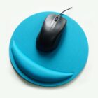 A black computer mouse rests on a round, bright blue mouse pad. The pad has a matching blue wrist rest in a semicircular shape at its bottom edge.
