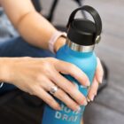 Close-up of hands holding a blue water bottle with a black lid and a silver ring on one finger.
