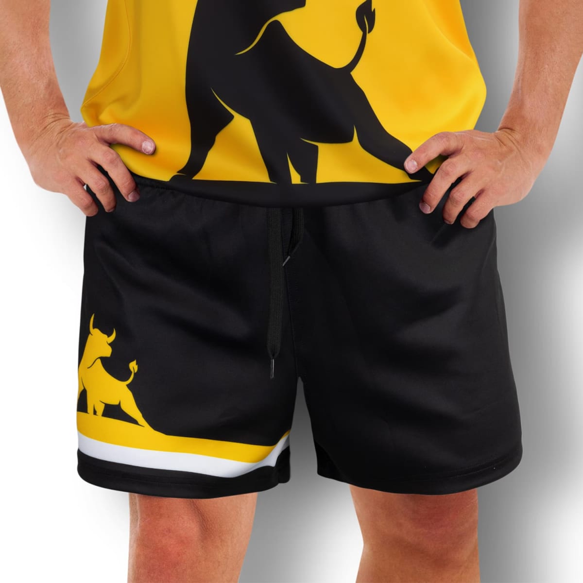 A person wearing a yellow shirt with a large black bull design and black shorts featuring a smaller, similar bull design. Their hands are on their hips, and they are standing against a plain white background.