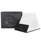 A white pyramid-shaped wireless speaker and charger with a mobile stand feature is placed in front of its box. The box displays an illustration and description of the device, highlighting its multifunctionality and light-up logo.