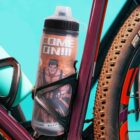 A water bottle with COME ON!!! and a muscular cartoon figure, mounted on a bike frame.