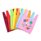 Colorful reusable shopping bags are spread out in a fan shape, featuring one pink bag with cute, cartoonish designs like flowers, clouds, and animals. The other bags are in solid colors: red, green, yellow, orange, and blue.