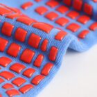 Close-up of a blue fabric with a pattern of raised, glossy red squares. The textured surface creates a sense of depth and contrast against the smooth, light background.
