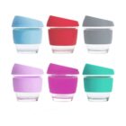 Six reusable glass cups with silicone lids and bands in various colors: light blue, red, gray, lavender, pink, and teal. The cups are arranged in two rows of three, each with a slightly tilted lid.