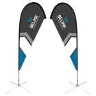 Two teardrop-shaped flags with BELINK COMMUNICATION text stand on cross-metal bases. The design includes gray, black, blue, and white geometric patterns.