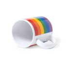 A white ceramic mug lying on its side with a rainbow stripe pattern wrapping around it. The colorful design spans from red to purple. The mug has a white handle and is set against a plain white background.