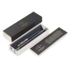 A blue Parker pen with silver accents is displayed in an open black and white box with the Parker logo. A folded paper is beside the box, featuring text about craftsmanship. The box cover is black with a gold Parker logo on top.