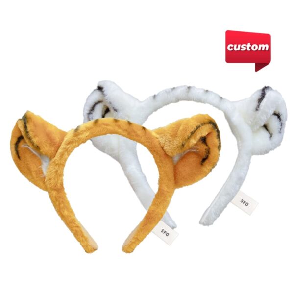 Two plush headbands with animal ears: one in orange-brown with black stripes resembling a tiger, the other in white with black stripes resembling a zebra. A custom label is in the top right corner. Tags attached to each headband.