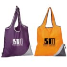 Two reusable bags are displayed: one purple and one orange. Both bags feature the logo and text shane michael engineering in black. Each bag has a small grey corner and integrated carrying handles.