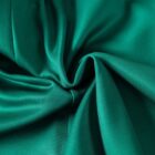 Close-up of emerald green fabric draped in soft, flowing folds, creating a swirl pattern. The texture appears smooth and silky, reflecting light gently, adding depth and richness to the color.
