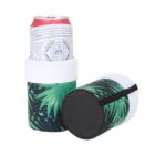 A soda can in a white and green leaf-patterned sleeve stands upright next to a similarly designed sleeve on its side, showing a black base. The sleeves have a white band at the top.
