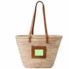 Woven straw tote bag with brown leather handles and a small leather patch featuring a green rectangle on one side.