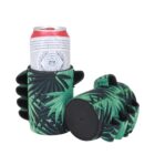 A red and white can is held in a black and green fingerless glove-shaped holder with a leaf pattern. Another identical holder is next to it, lying on its side, showing the bottom part.