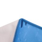 Close-up of the corner of a cloth or fabric, showing a split between a white side and a blue side with a dark blue stitched edge. The blue side has faint geometric patterns and small dark markings.