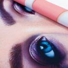 Close-up of a rolled poster showing a detailed image of a persons blue eyes with dark makeup. The poster is rolled slightly, revealing its thickness and texture. The colors are vivid and the focus is on the eyes.