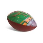 A football featuring a printed image of a marching band forming the letter T on a football field, with a stadium full of spectators in the background. The ball rests on a white surface.