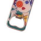 A colorful bottle opener featuring a cartoon-style illustration of a person with a decorative headpiece and red lips. The persons hand is near their mouth, and theres a swirl design over one eye.