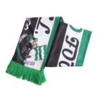 A football scarf with green fringe, featuring a cartoon character and the text SHINSHU MATSUMOTO FOTBALL. The scarf has green, black, and white sections with bold lettering and graphics.
