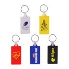 Five colorful keychains: white with a logo, yellow with a black squiggle, red with Pist Idiots in a heart, blue with Newcastle Coal, and black with HiSpec in yellow font, each featuring a metal ring.