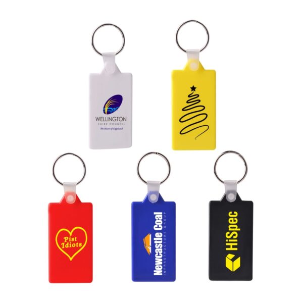 Five colorful keychains: white with a logo, yellow with a black squiggle, red with Pist Idiots in a heart, blue with Newcastle Coal, and black with HiSpec in yellow font, each featuring a metal ring.