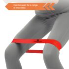 A person wearing light gray leggings demonstrates an exercise with a red resistance band looped above their knees. An arrow points to the band with text saying, Can be used for a range of exercises.