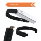 Fitness tracker showing a removable USB module for charging. The black band is open, and the module, partially detached, is shown with a close-up of the USB connector. An orange arrow points to the charging port.
